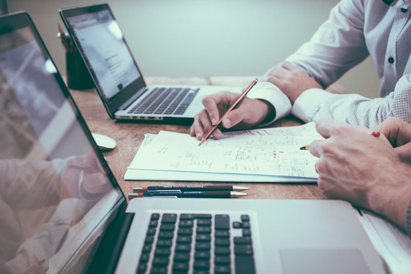 Personas revisando un plan de trabajo en papel junto a computadoras portátiles